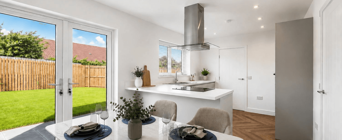 Modern open-plan kitchen and dining area with white cabinets, breakfast bar, and French doors leading to a garden