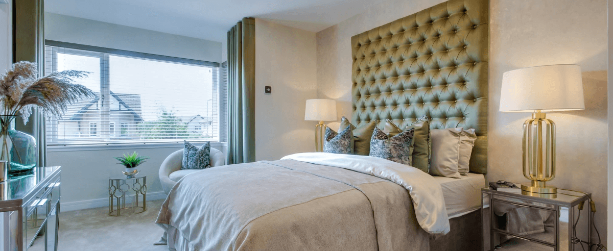 Modern bedroom in a new-build home featuring an olive green tufted headboard, gold lamps and a window with blinds