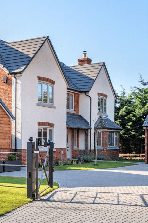 Modern new-build house with white render and red brick detailing, featuring a block-paved driveway and metal gate