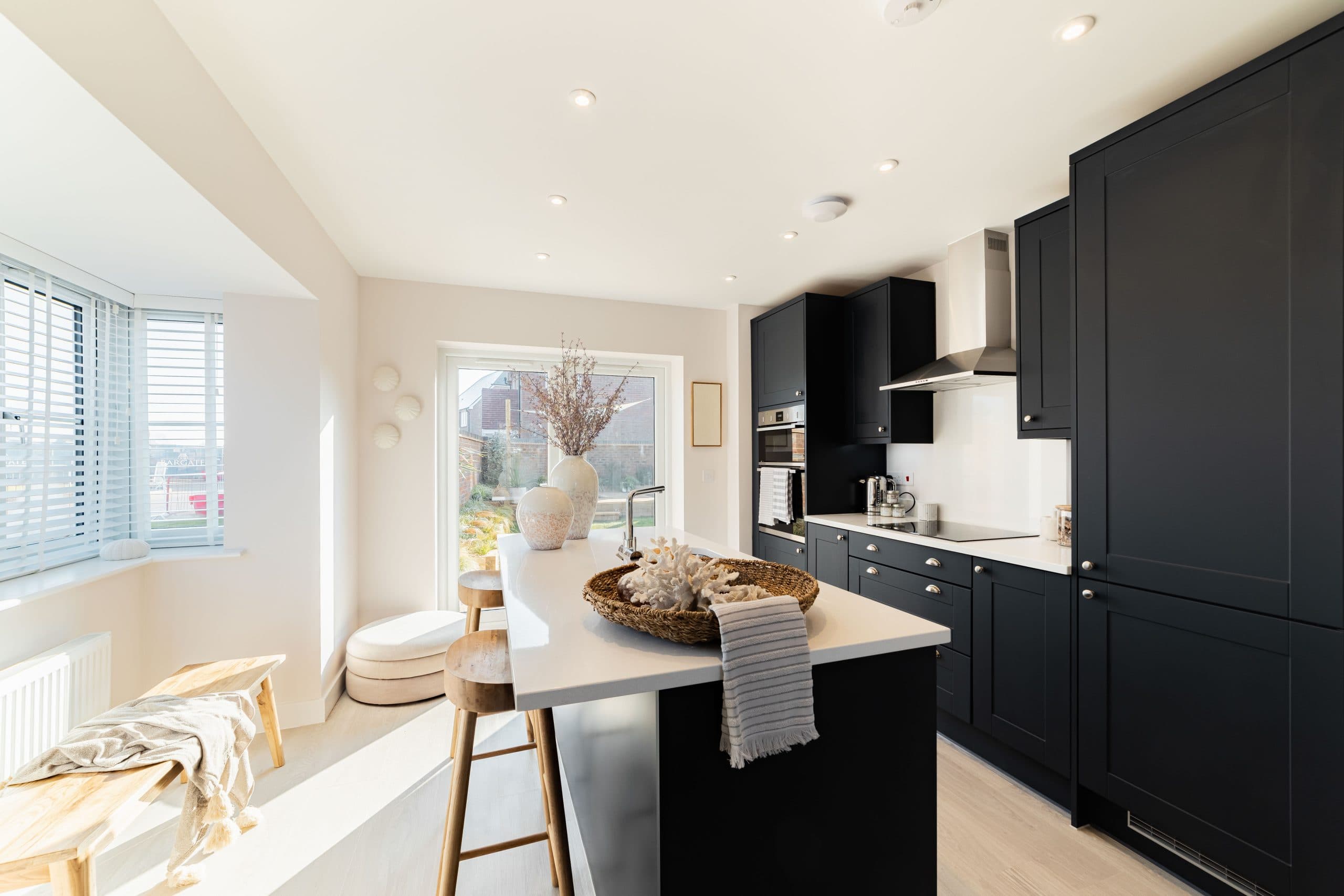Modern kitchen interior with navy cabinets, white quartz island, wooden bar stools and a bay window seat area