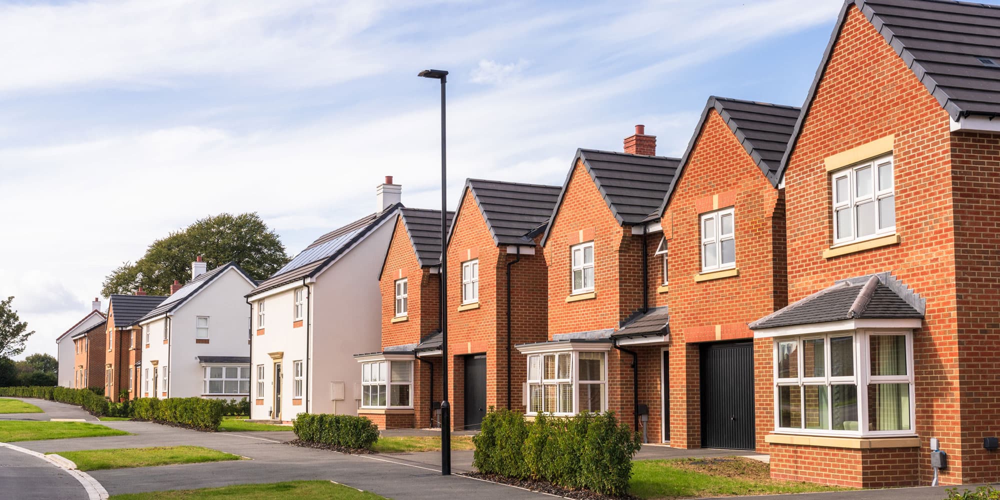 Row of modern red-brick and white-rendered detached new-build houses in a quiet residential street