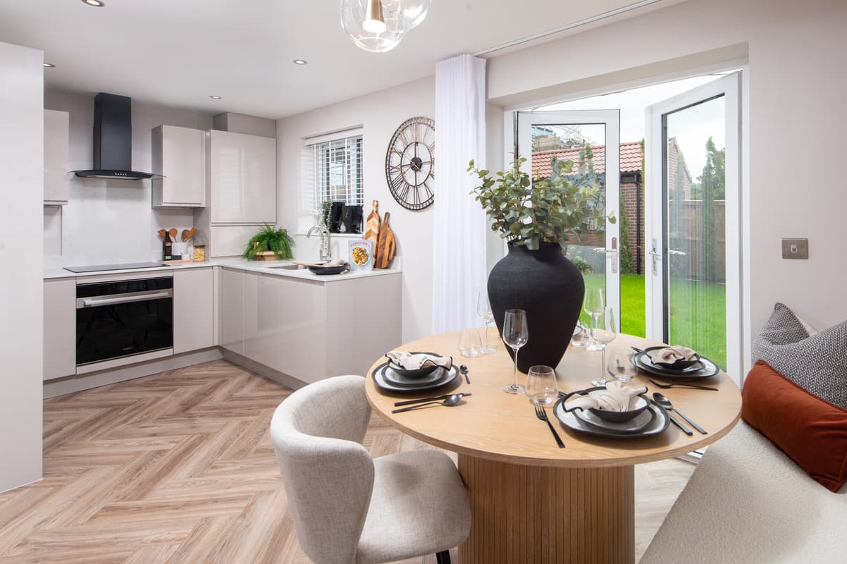 Modern open-plan kitchen and dining area in a new-build home with a wooden table, herringbone flooring, and garden doors