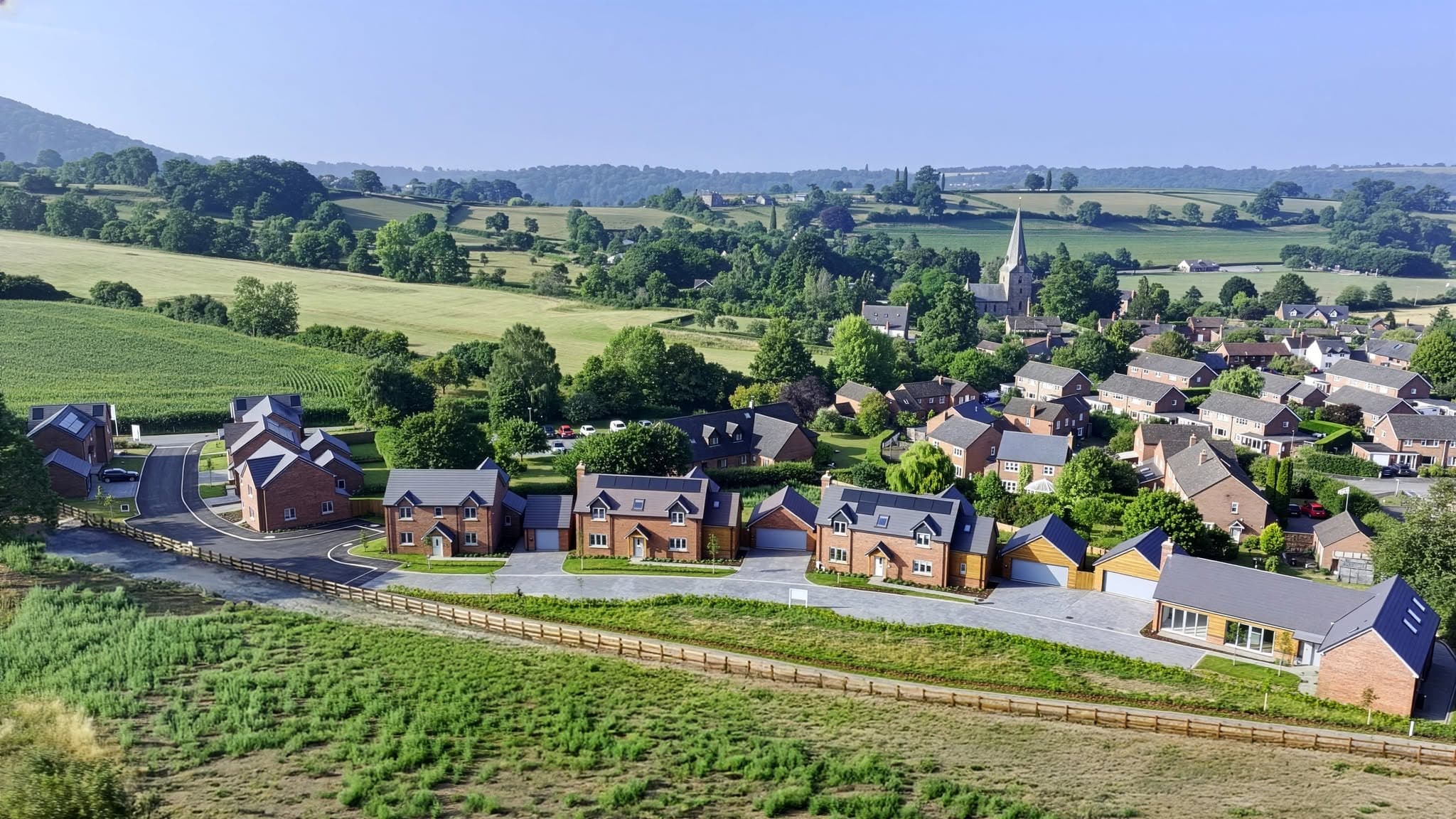 Aerial view of a new-build red brick housing development set within a rural British landscape with a village church