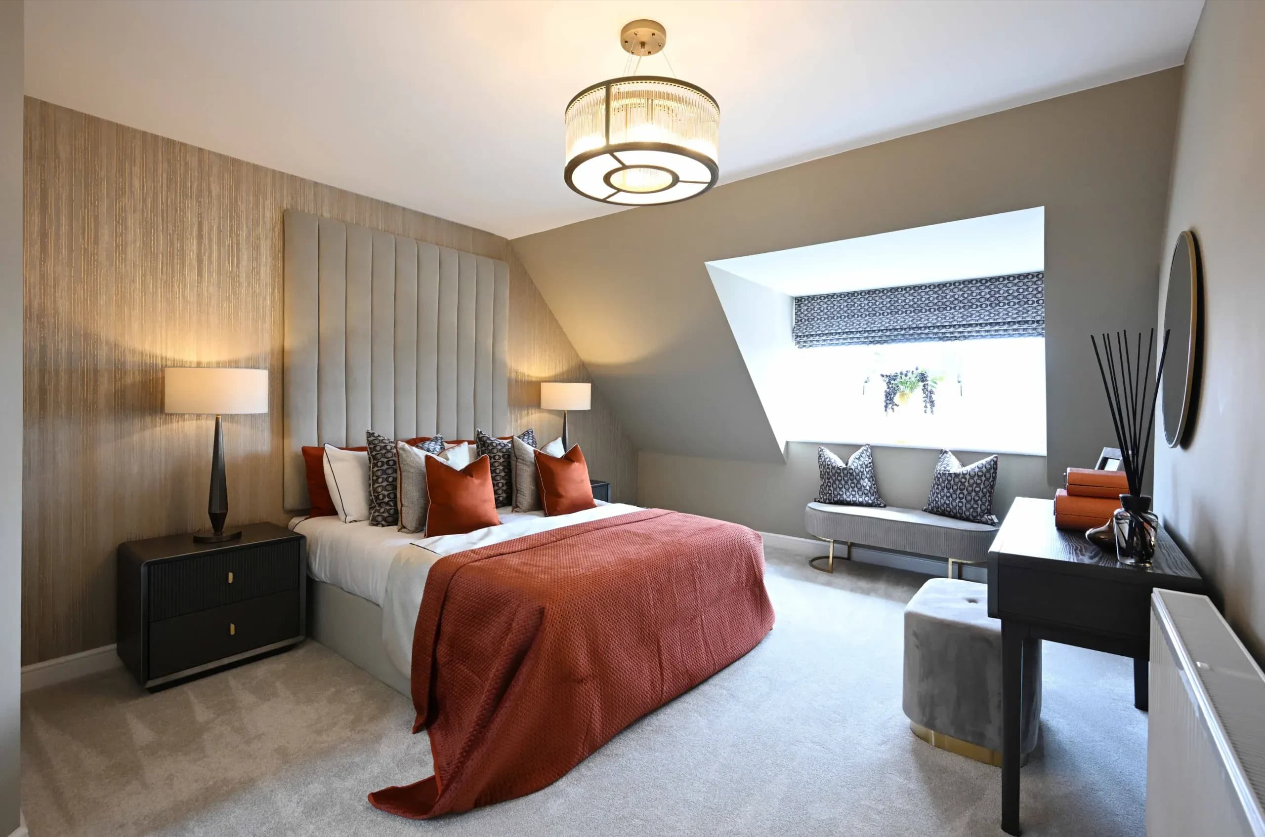 Modern bedroom interior with a feature headboard, burnt orange bedding, a sloped ceiling, and a dormer window seat