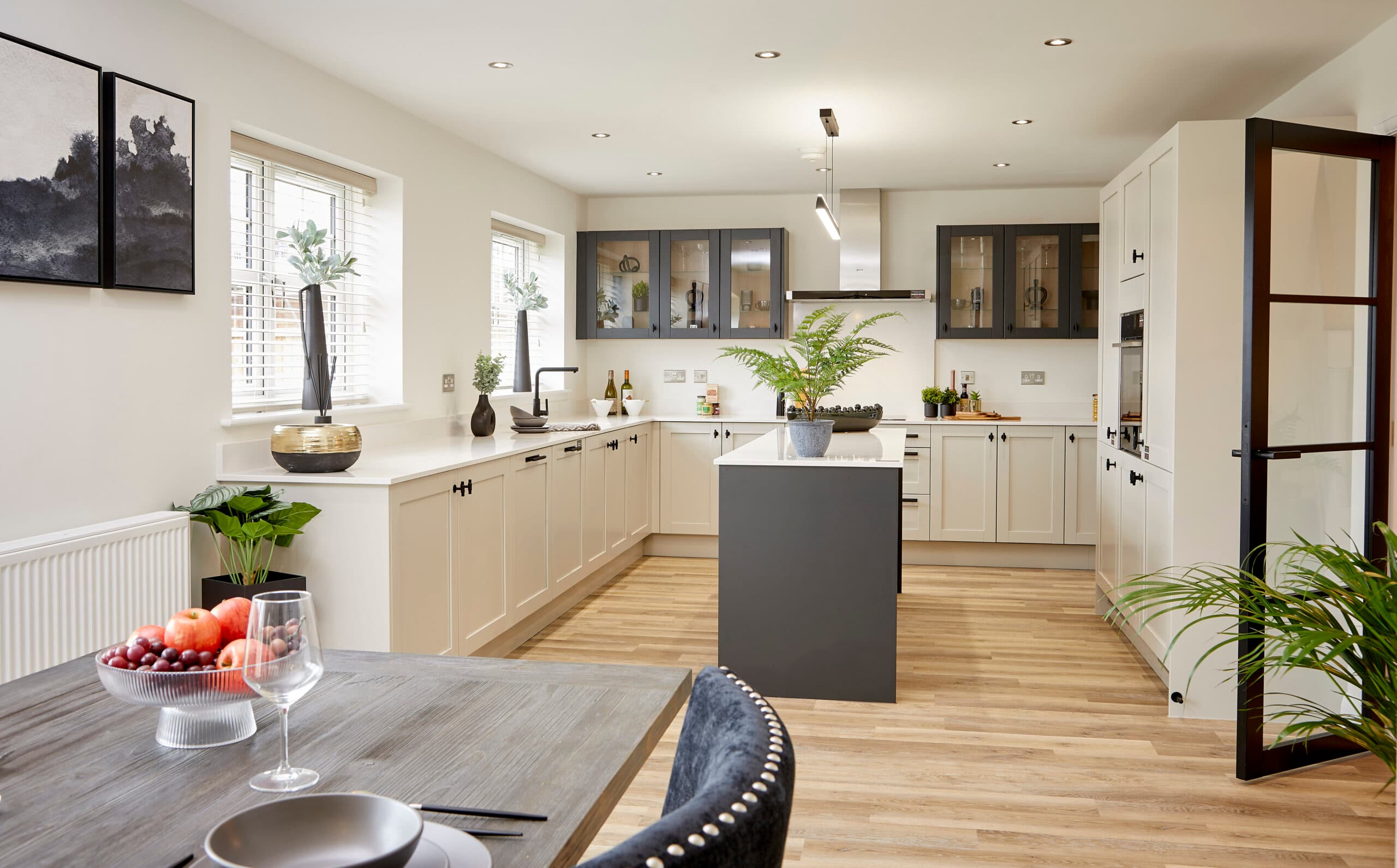 Modern open-plan kitchen with cream cabinets, a dark grey island, wood flooring, and a dining table in the foreground