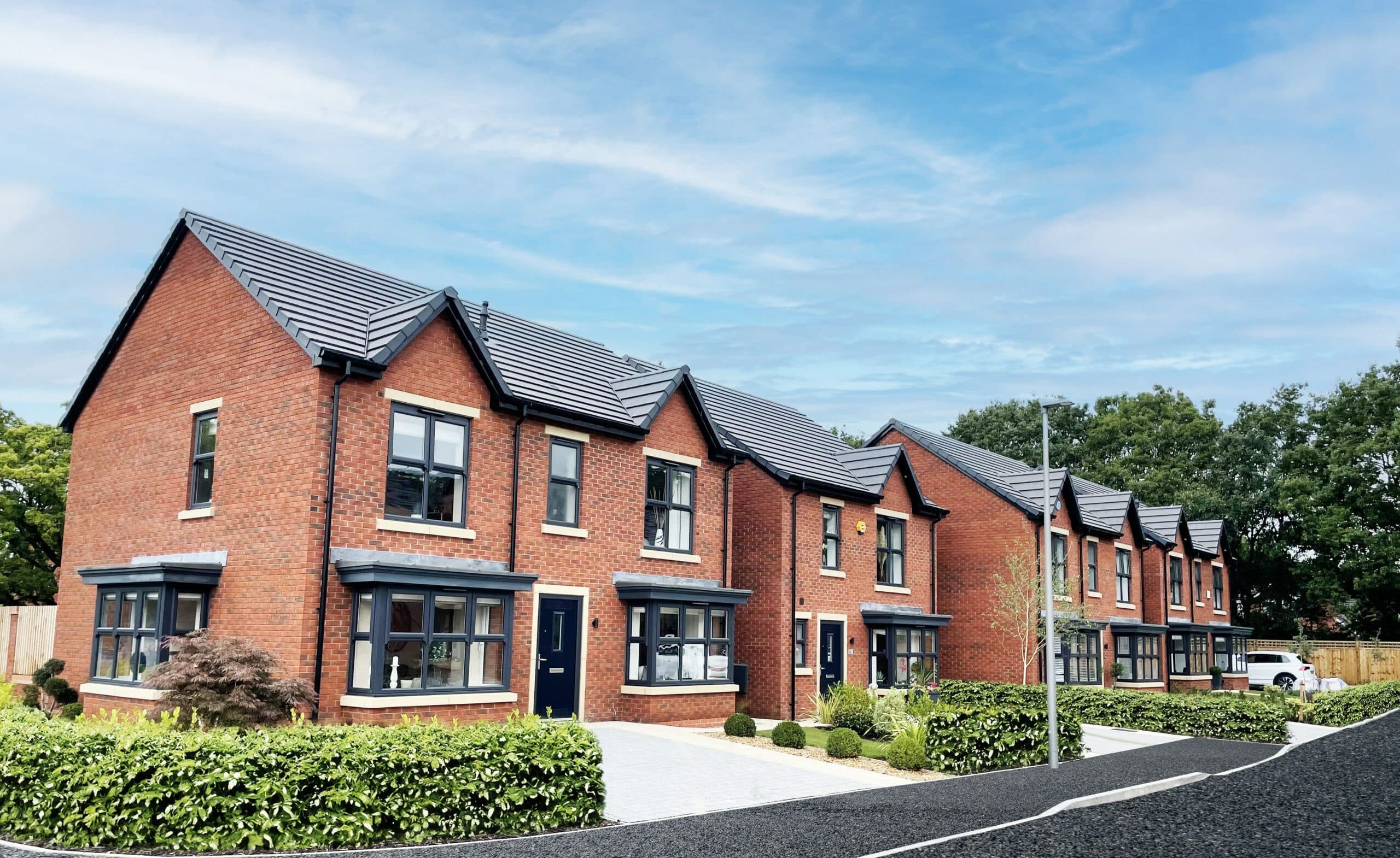 Row of modern red brick semi-detached houses with grey roof tiles and bay windows under a blue sky