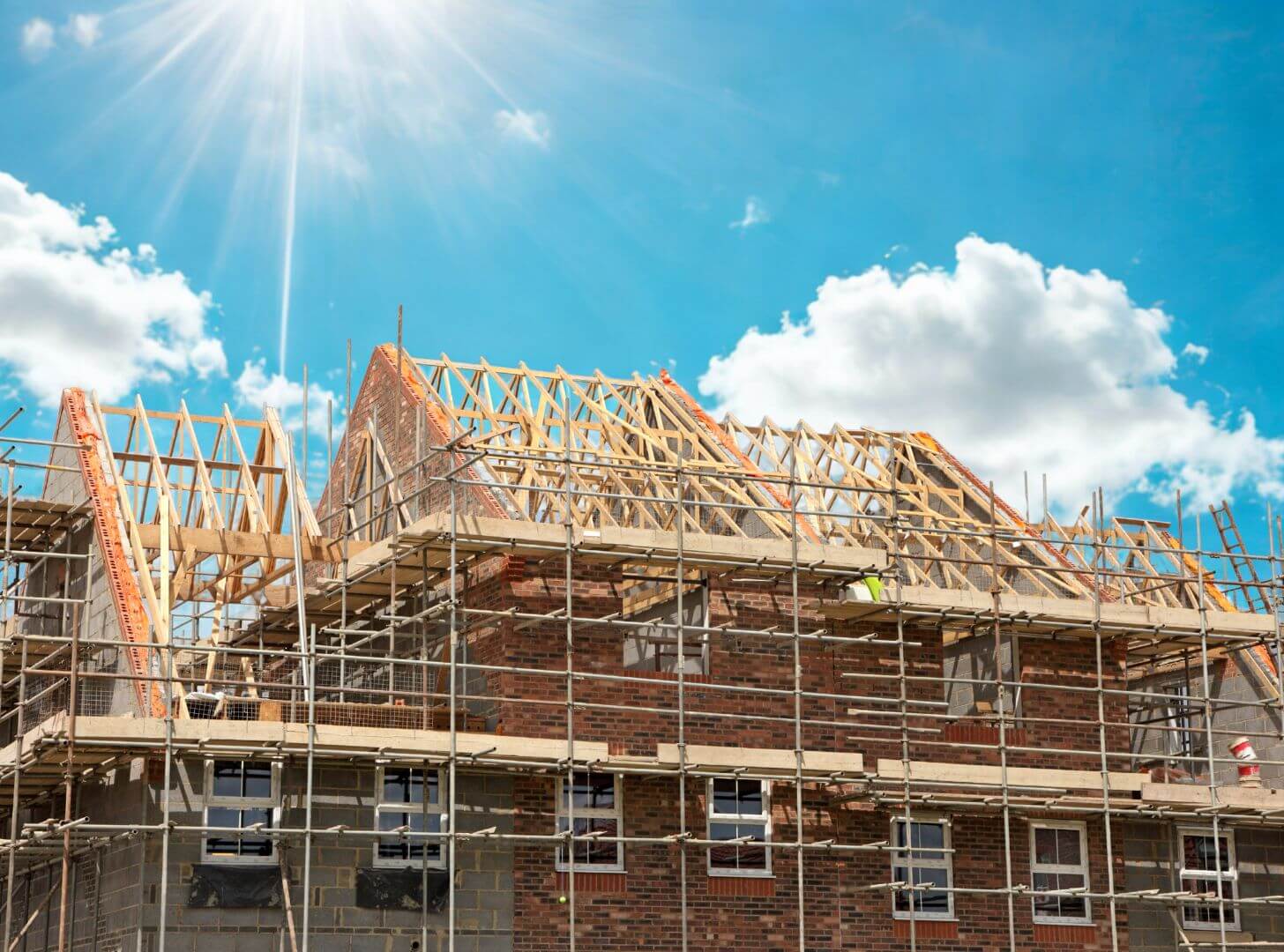 Construction site of a new brick house under development with timber roof trusses and scaffolding against a sunny sky