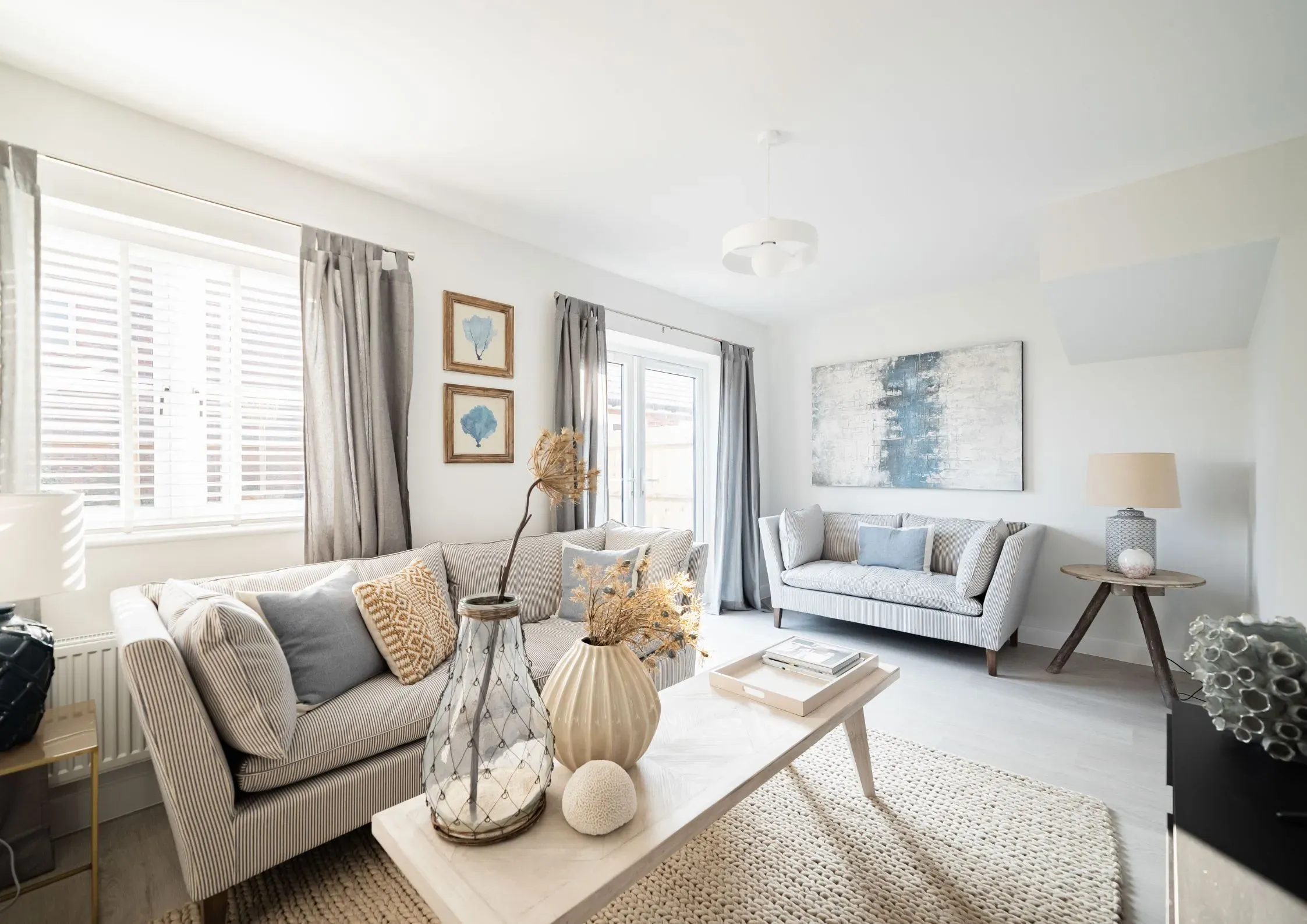 Bright, neutral-toned living room in a new-build home featuring striped sofas, a coffee table with decor and a rug