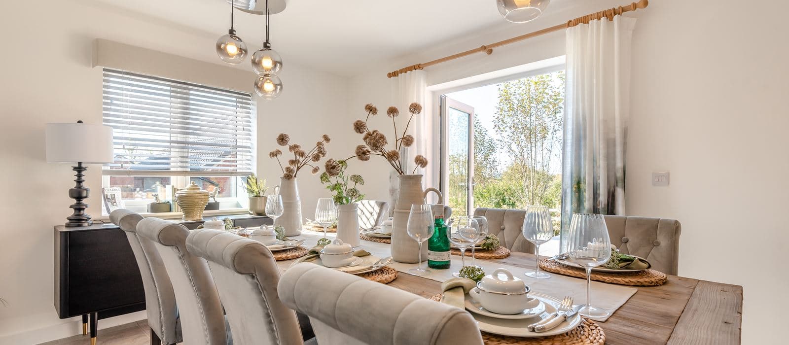 Bright dining room in a new-build home with a wooden table, grey upholstered chairs, and open doors to the garden