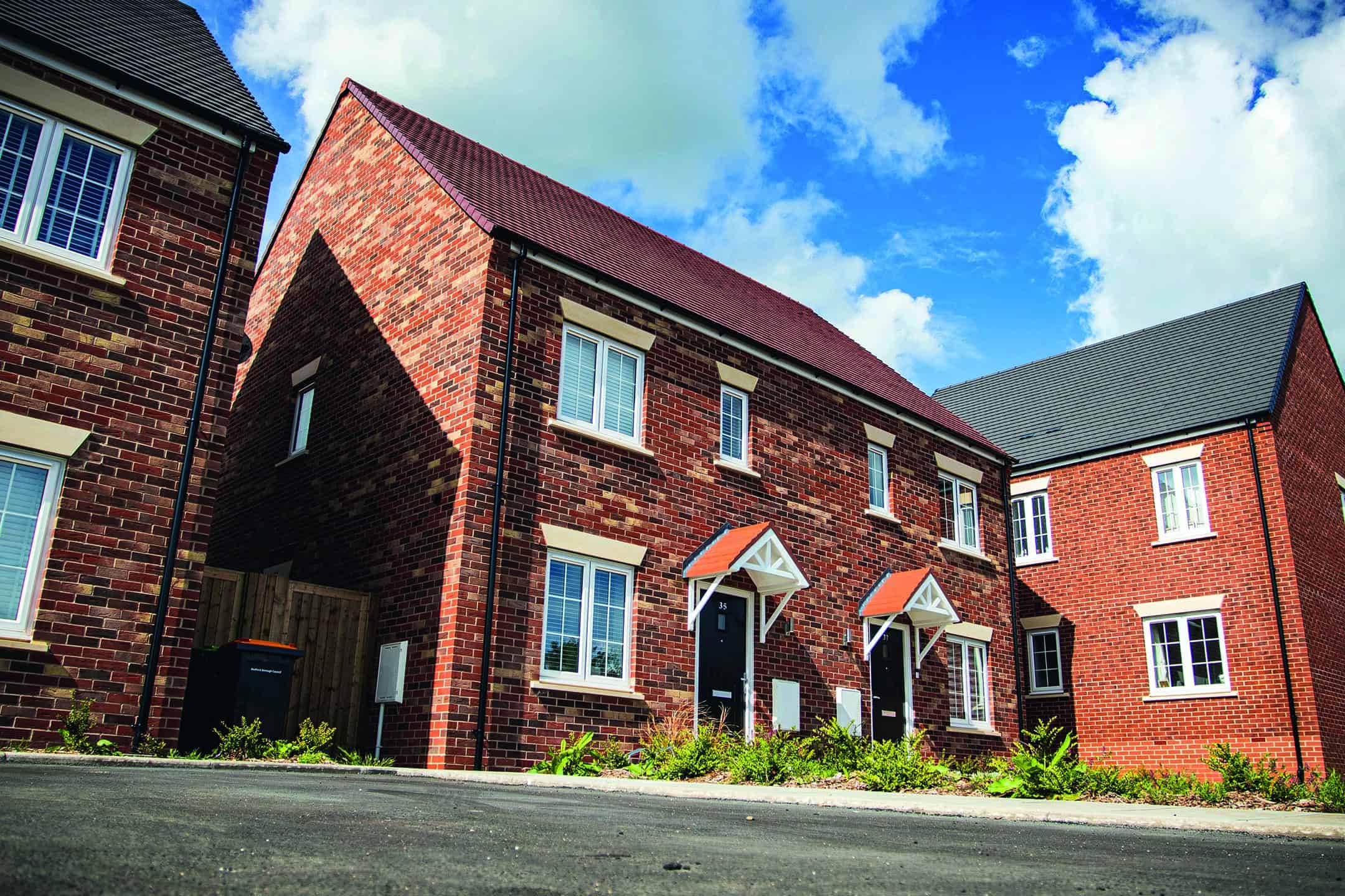 Modern red-brick semi-detached new-build homes under a blue sky