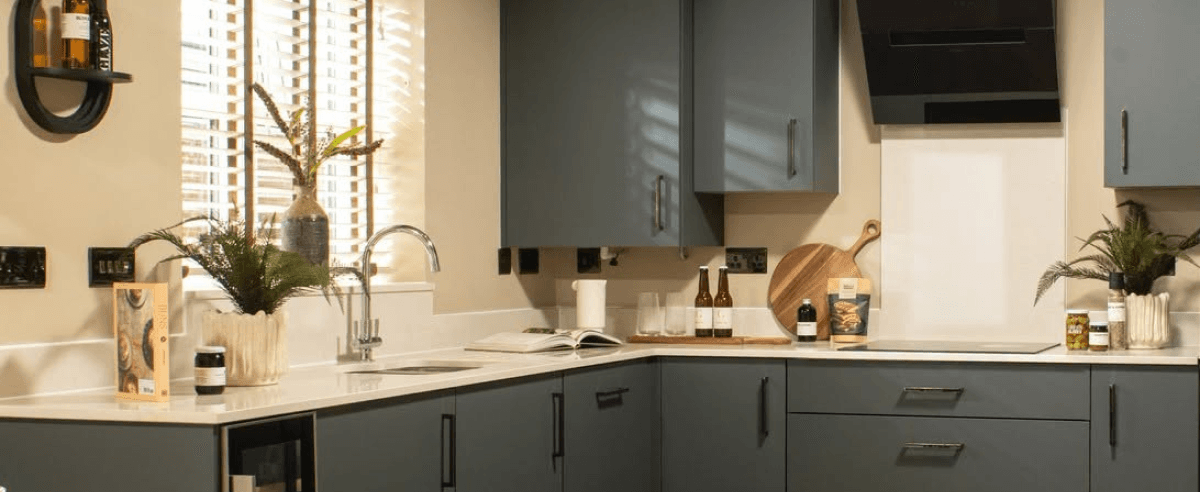 Modern kitchen with blue-grey cabinets, light countertops, integrated appliances, and a window with venetian blinds
