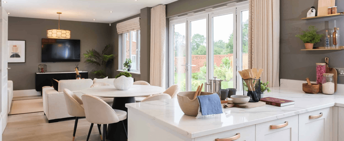 Open-plan kitchen and living area in a new-build home with marble-effect surfaces and bifold doors to the garden