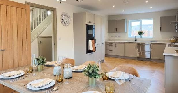 Modern open-plan kitchen and dining area in a new-build house with light grey cabinets and wooden herringbone flooring