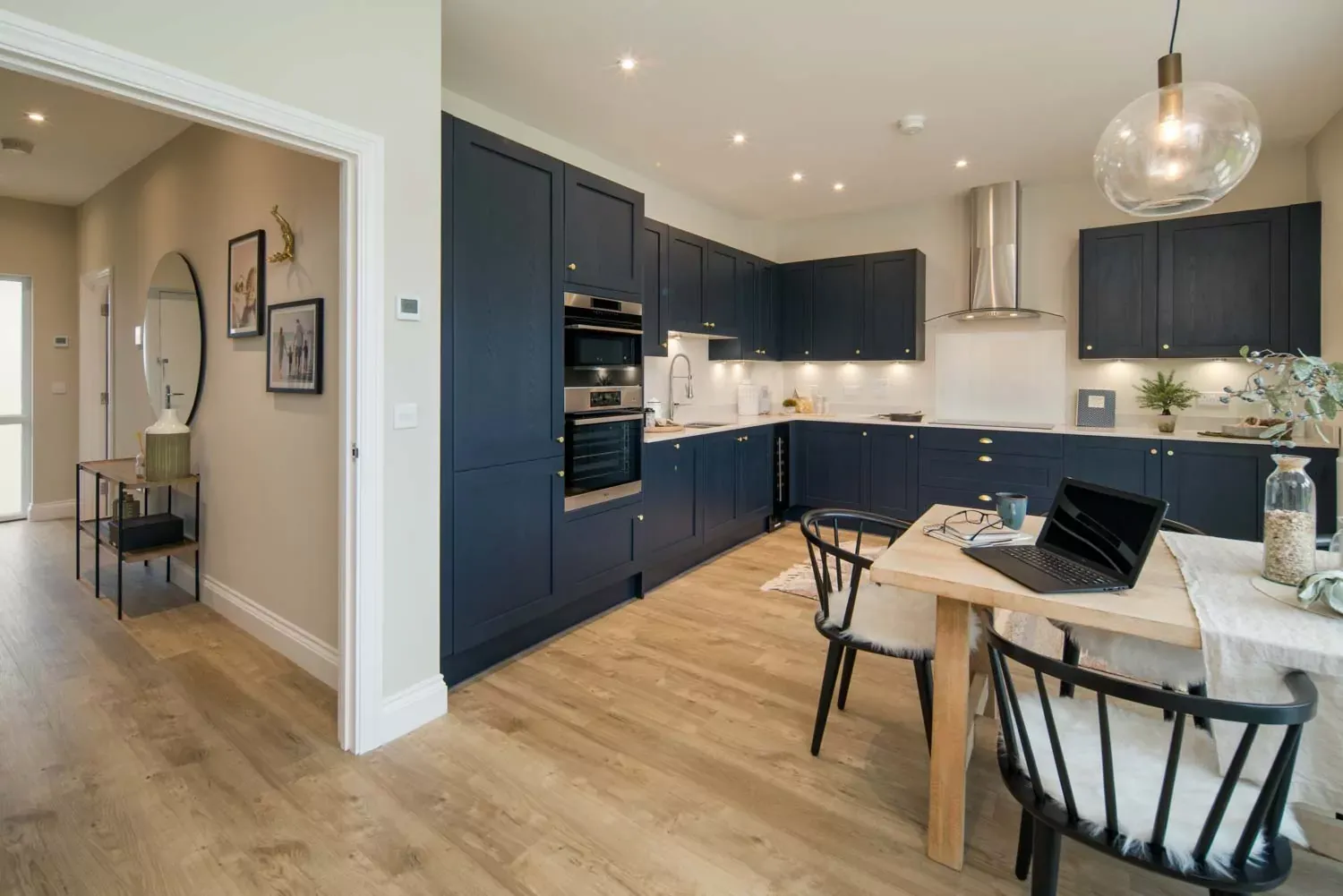 Modern open-plan kitchen with navy blue cabinets, wooden flooring, and a dining area with black spindle chairs