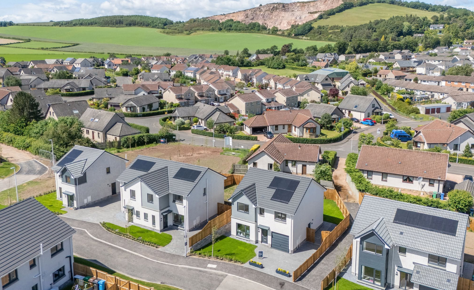 Aerial view of a residential new-build housing development with solar panels on slate roofs and surrounding greenery